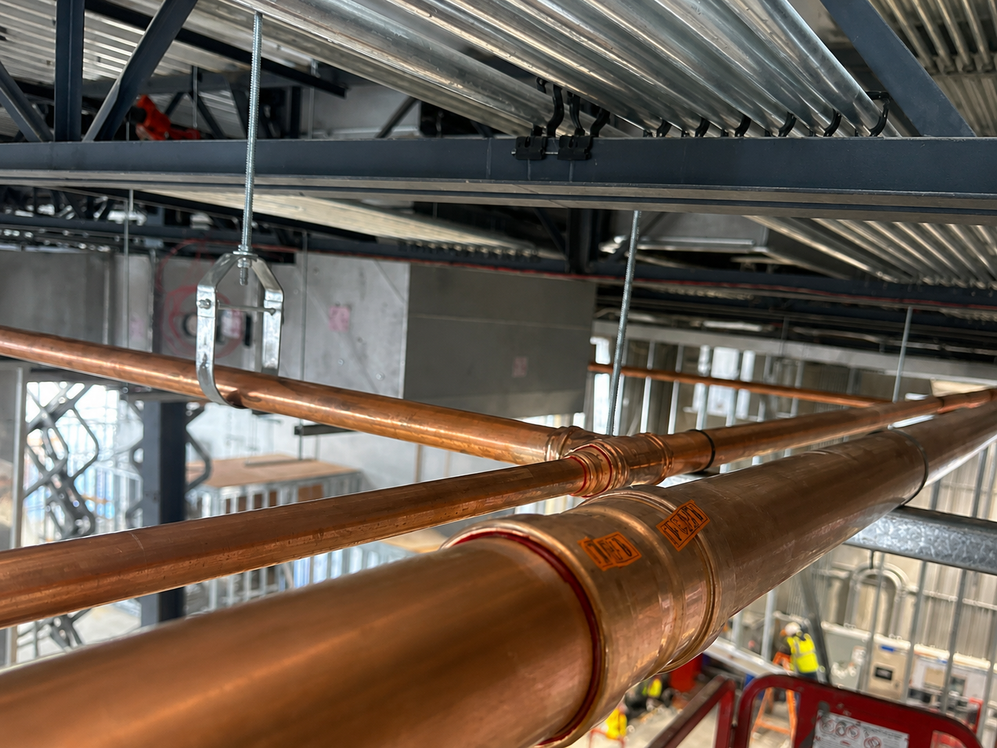 Large-diameter overhead copper water distribution mains suspended from structural steel at BJ's Wholesale Club, Selma NC